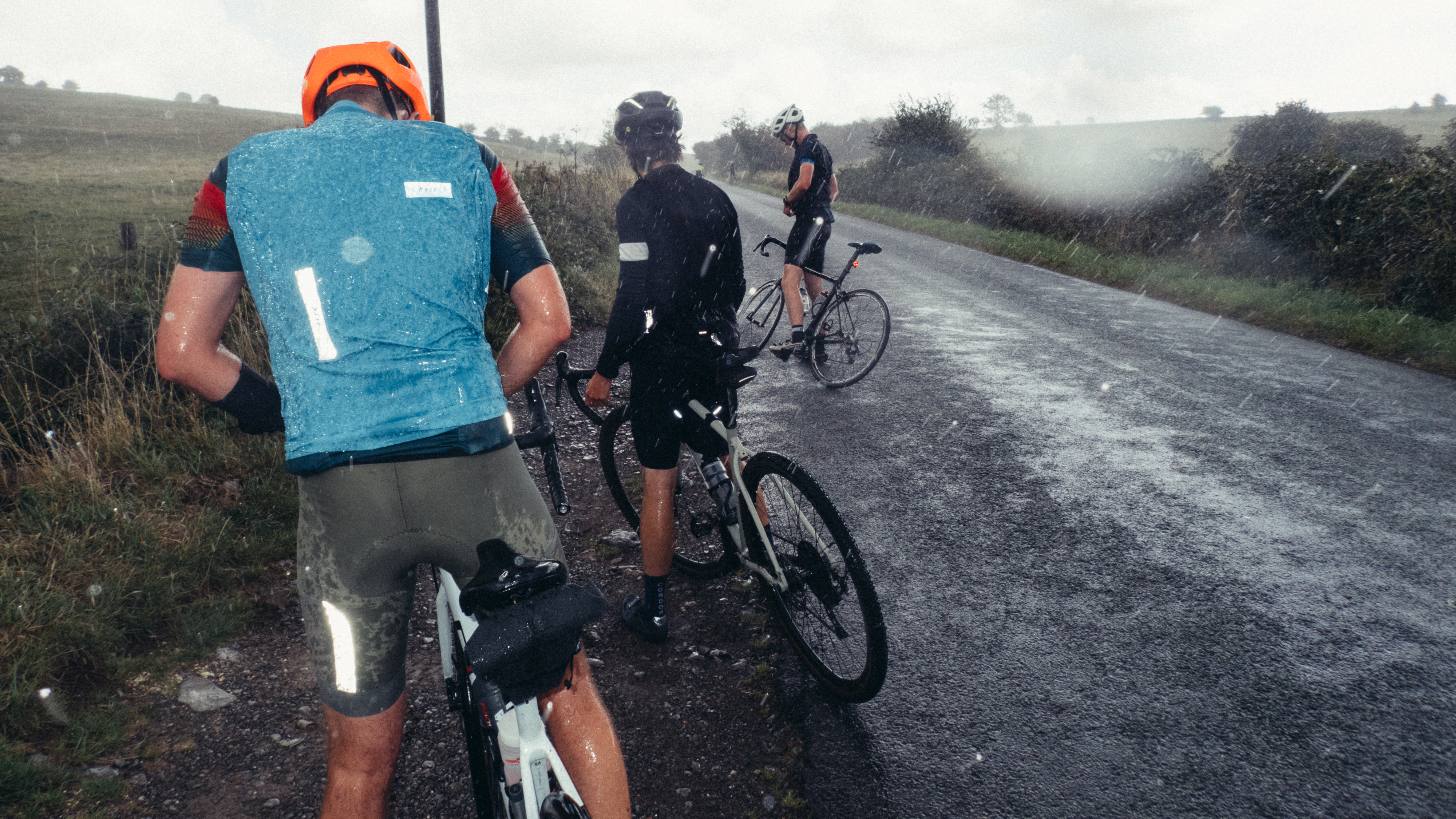 A downpour on a hilltop with cyclists rushing to put jackets on
