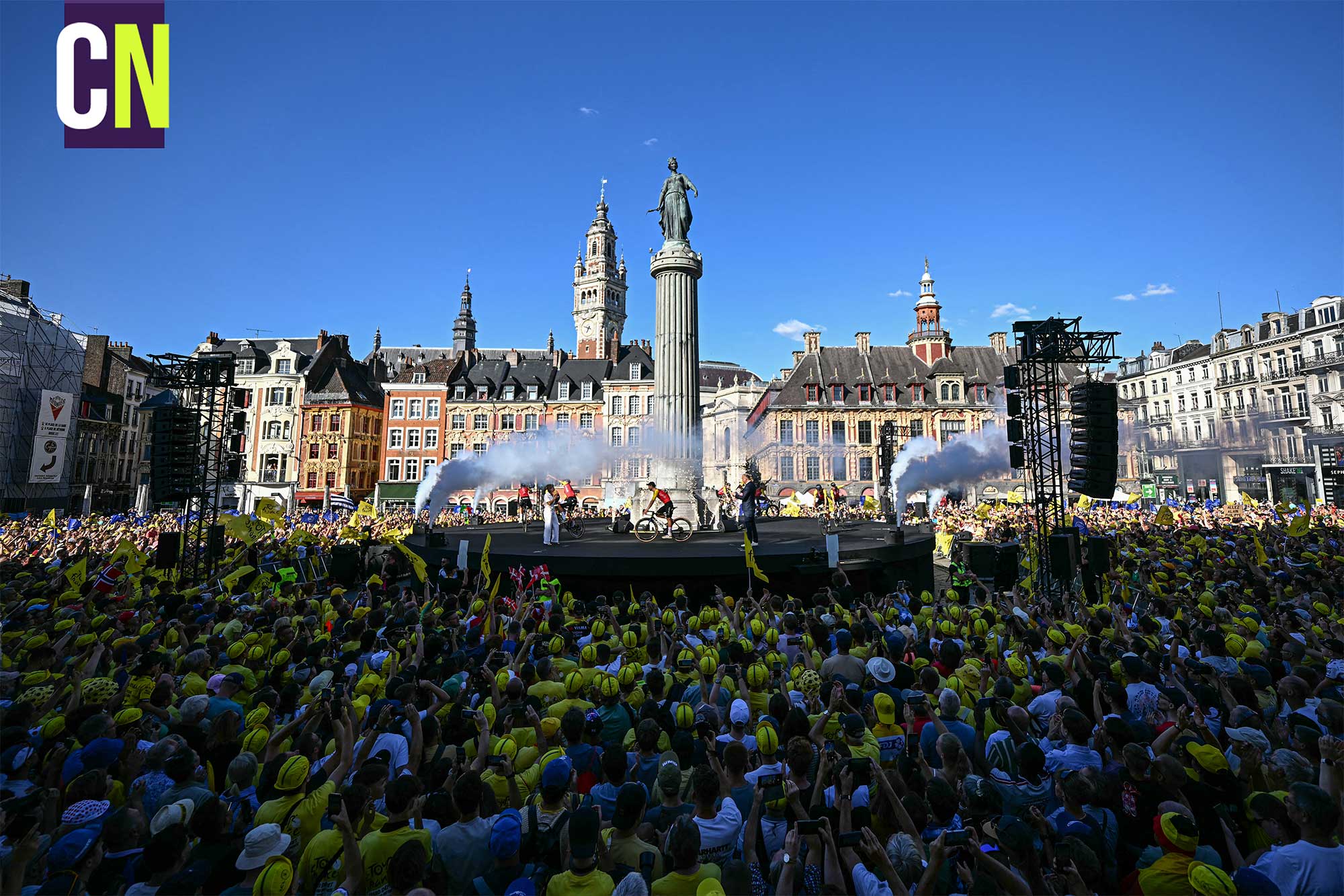 Fans hold yellow Tour de France flags ahead of the official teams presentation, days prior to the start of the 112th edition of the Tour de France cycling race, at Grand Place with a view of the Colonne de la D&eacute;esse monument and the the tower of the Vieille Bourse de Lille building, in Lille, northern France, on July 3, 2025. (Photo by Loic VENANCE / AFP) (Photo by LOIC VENANCE/AFP via Getty Images)